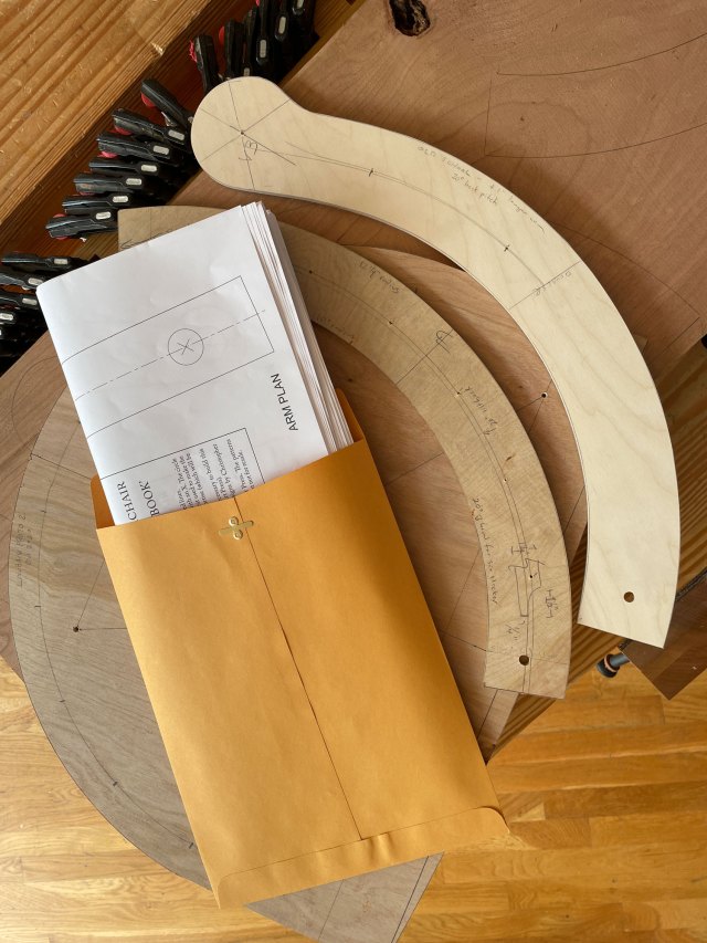 Folded printed plans for chairs inside a manila envelope on a workbench. Chair patterns sit next to the envelope.