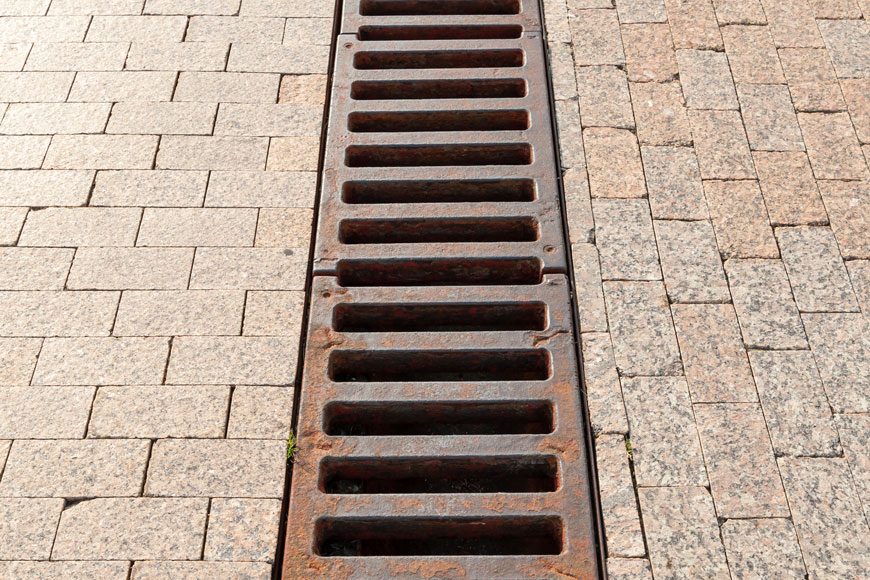 A raw cast iron trench grate with an industrial slatted look separates brickwork laid in two different orientations