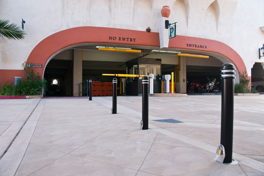 A line of black posts with annular rings are locked with padlocks in front of a parking garage