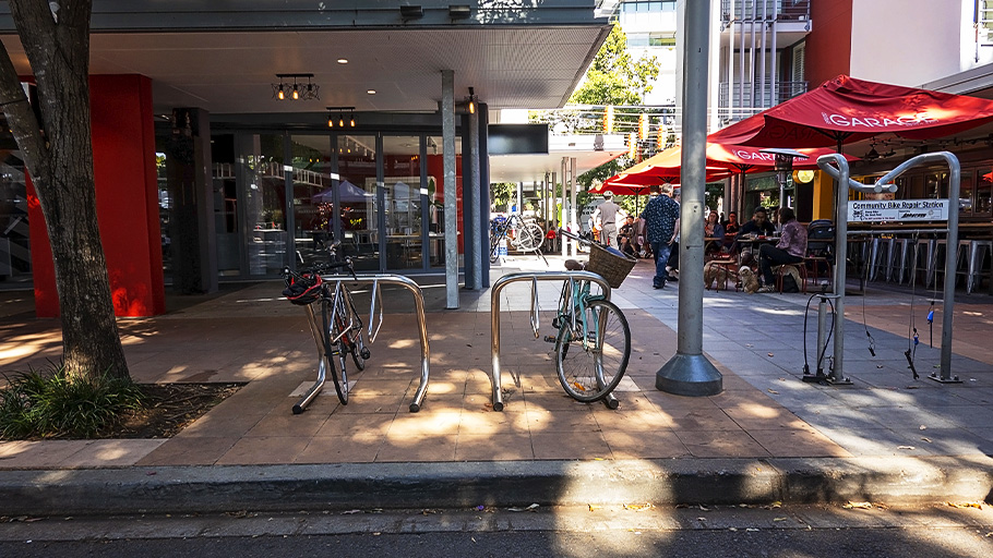 Arched bike racks sit outside of a business complex with patrons seated at the bike repair station