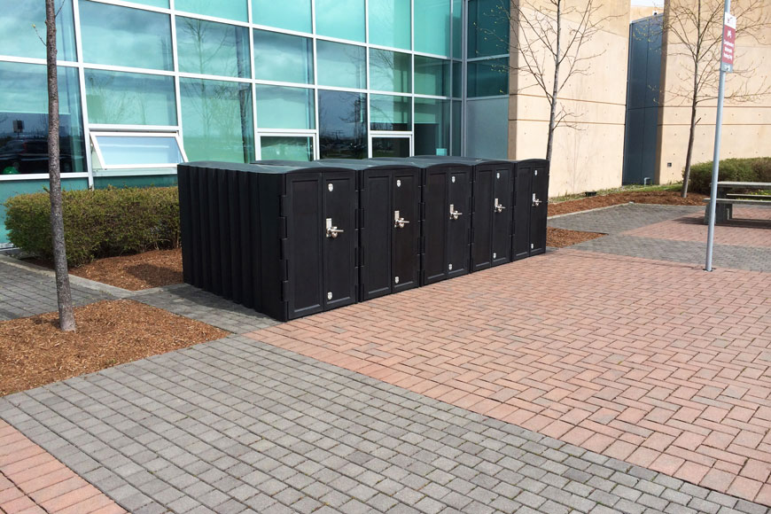 A row of bike storage lockers sit outside a building.