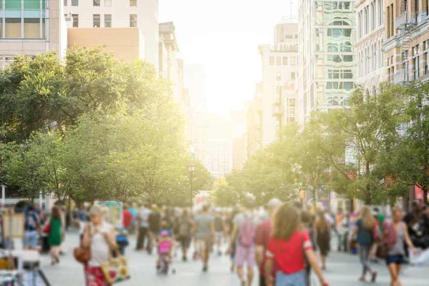 A blurred image shows a busy park in Manhattan with sunlight peeking through the buildings behind.