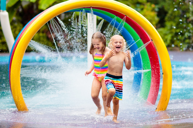 Two happy children play in water spray in a park filled with colorful bent tubes.