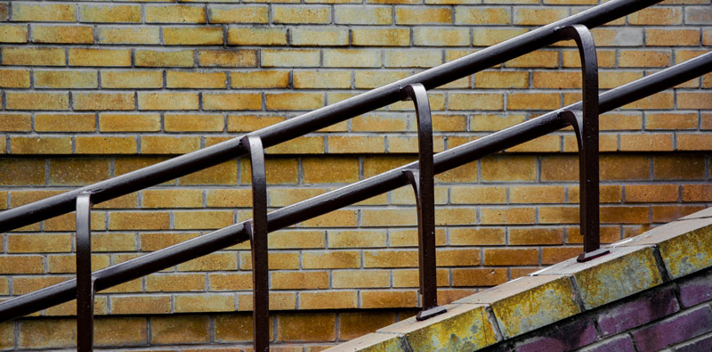 A brown powder-coated railing made of brown square and round tubing before a yellow brick wall