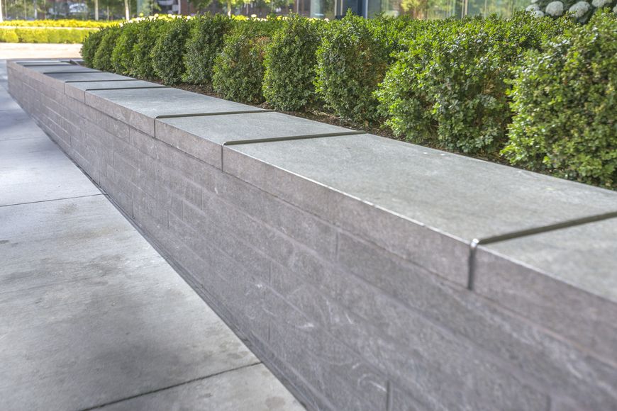 A low grey stone wall with bushes in the background