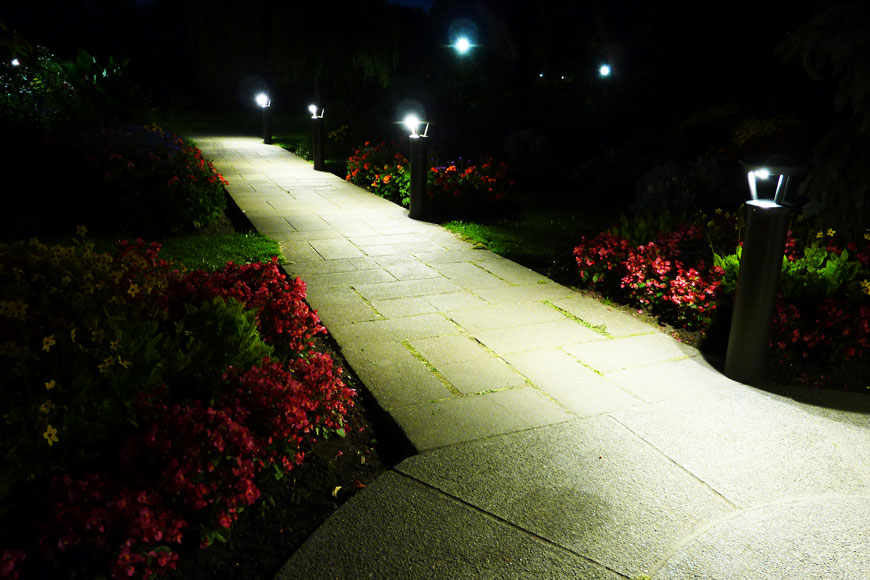 Solar lighting bollards illuminate a flower-bordered path at night