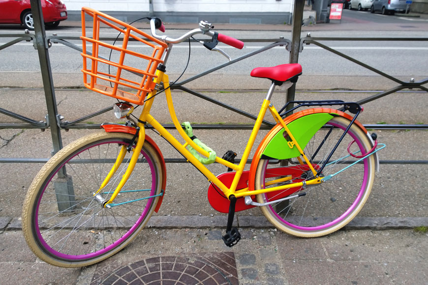 Bicicleta pintada de varios colores aparcada en la calle.