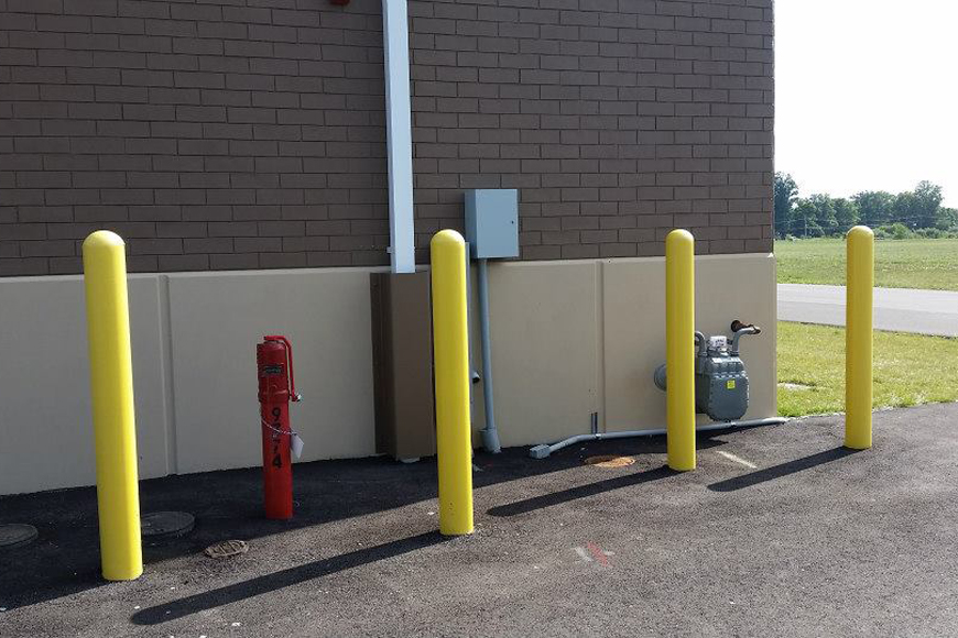 Concrete bollard caps and steel pipes are painted yellow, protecting exposed utilities