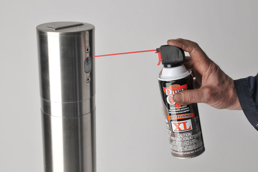 A can of lubricant with a red straw is held against a white background