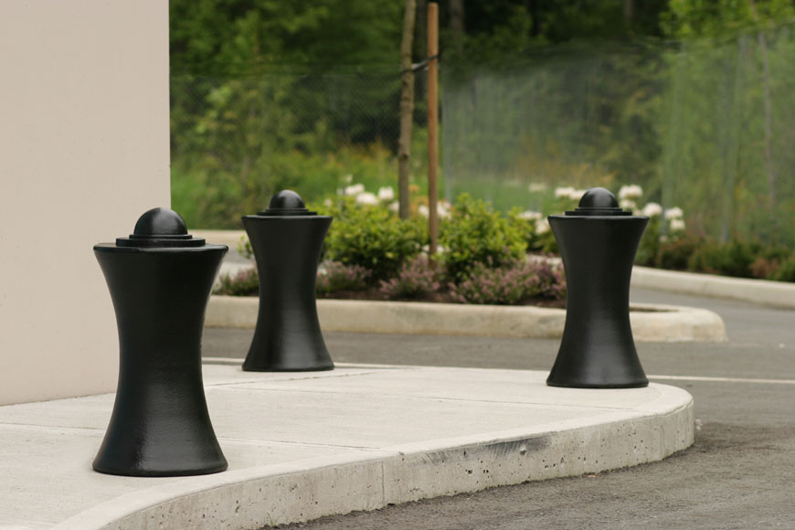 Three beautiful maritime bollards guard the corner of a sidewalk: plantings in the background