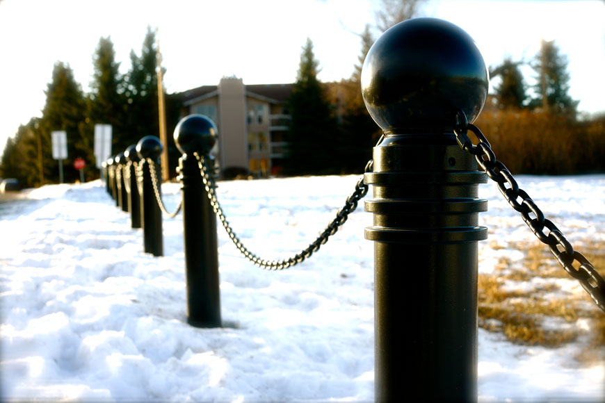 A line of dark bollards stand in the snow, connected with draping chains