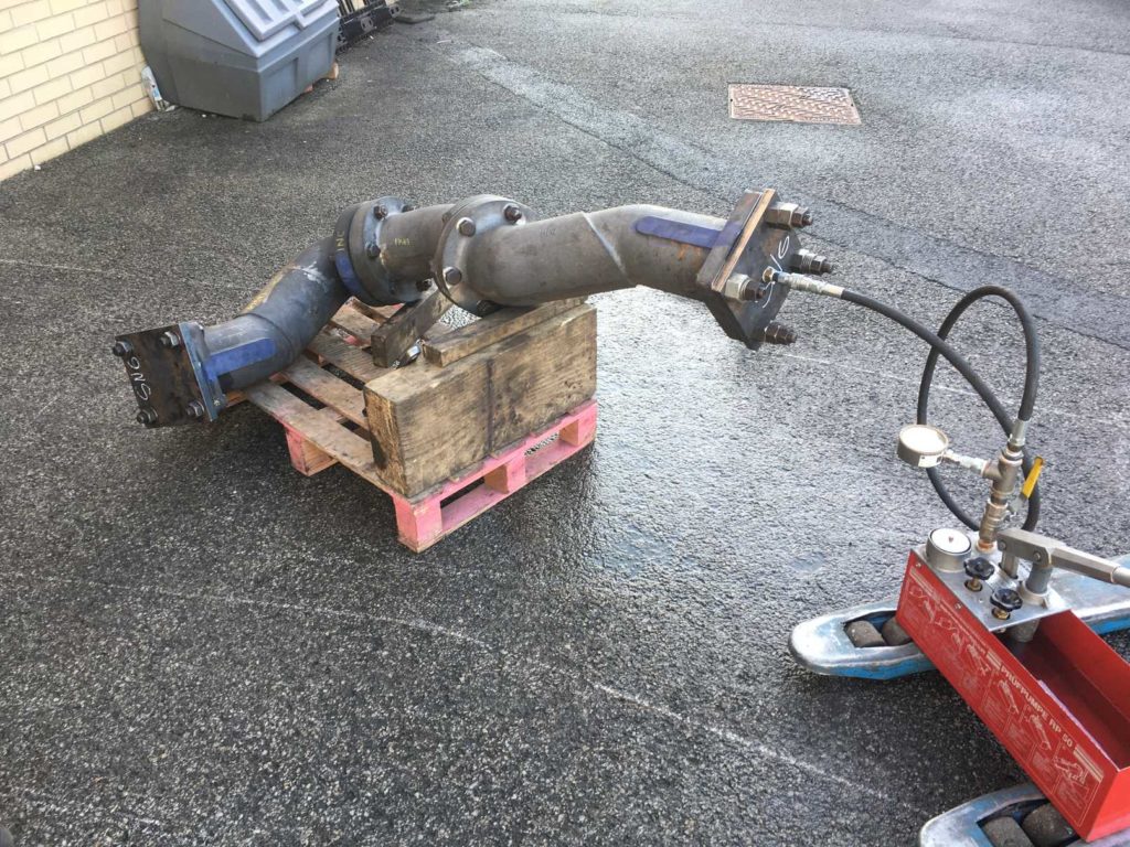 Grey steam pipes sitting on a wooden crate, attached to a pressure gauge